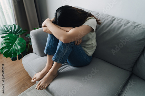 Unhappy lonely depressed woman is sitting on the couch and covering her face with her hands