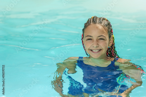 Smiling cute litte girl with colorful braids in her hair  is standing in the pool. Horizontally. 