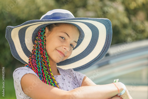 Relaxed little girl is posing in a straw hat  outdoors. Horizontally. 