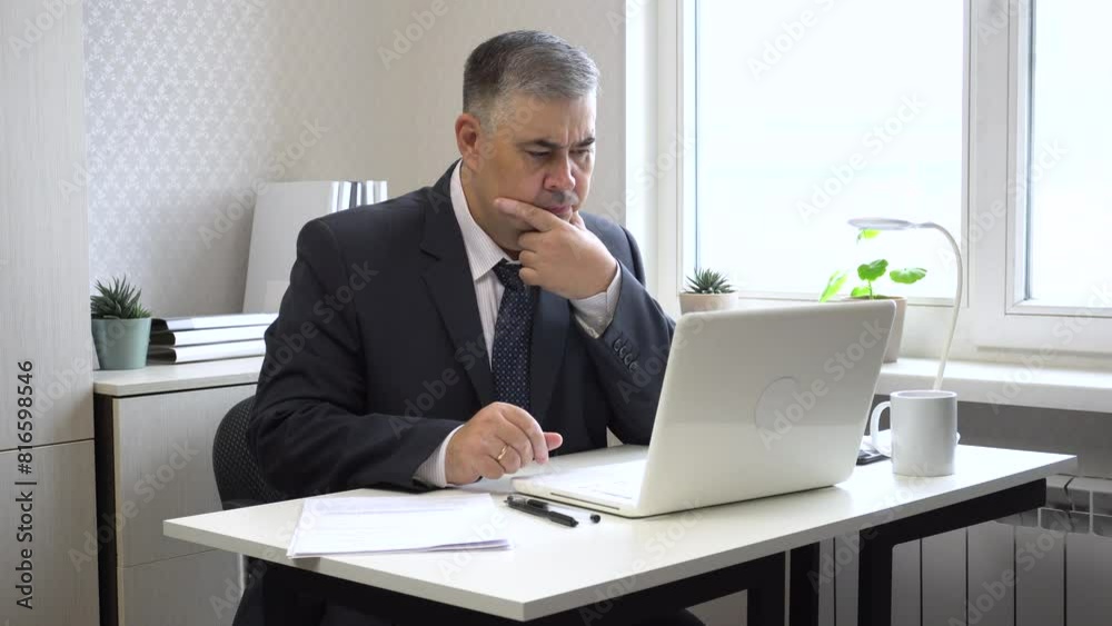 Businessman in suit and tie working in office environment. He types on computer, then pauses to contemplate and carefully examines computer screen. Ideal for content about office work, business manage Businessman in suit and tie working in office environment. He types on computer, then pauses to contemplate and carefully examines computer screen. Ideal for content about office work, business manage