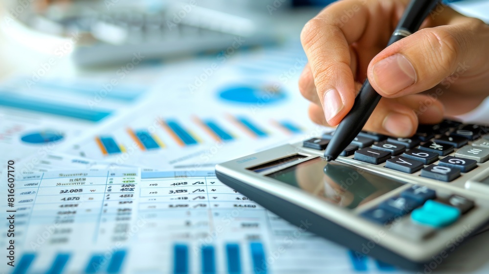 A close-up of a hand holding a calculator next to financial documents A close-up of a hand holding a calculator next to financial documents