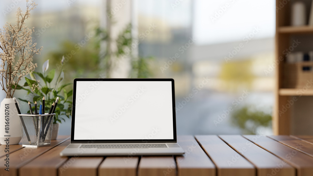 A front view of a laptop computer mockup and decorative objects are on a wooden tabletop in a room. A front view of a laptop computer mockup and decorative objects are on a wooden tabletop in a room.