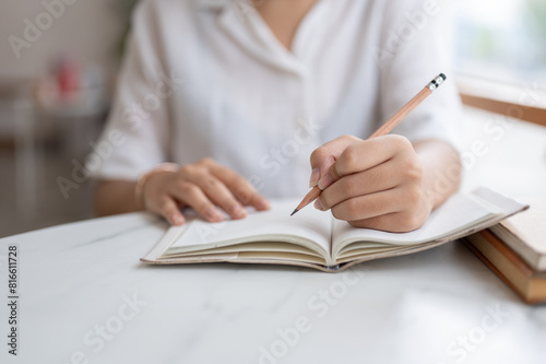 A cropped shot of a woman writing something in her notebook while sitting in a coffee shop.