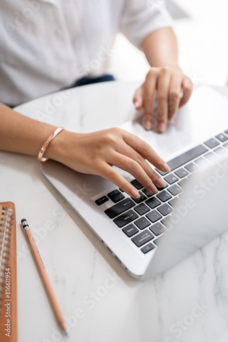 A close-up image of a woman typing on keyboard, working on the computer at a table in a coffee shop.