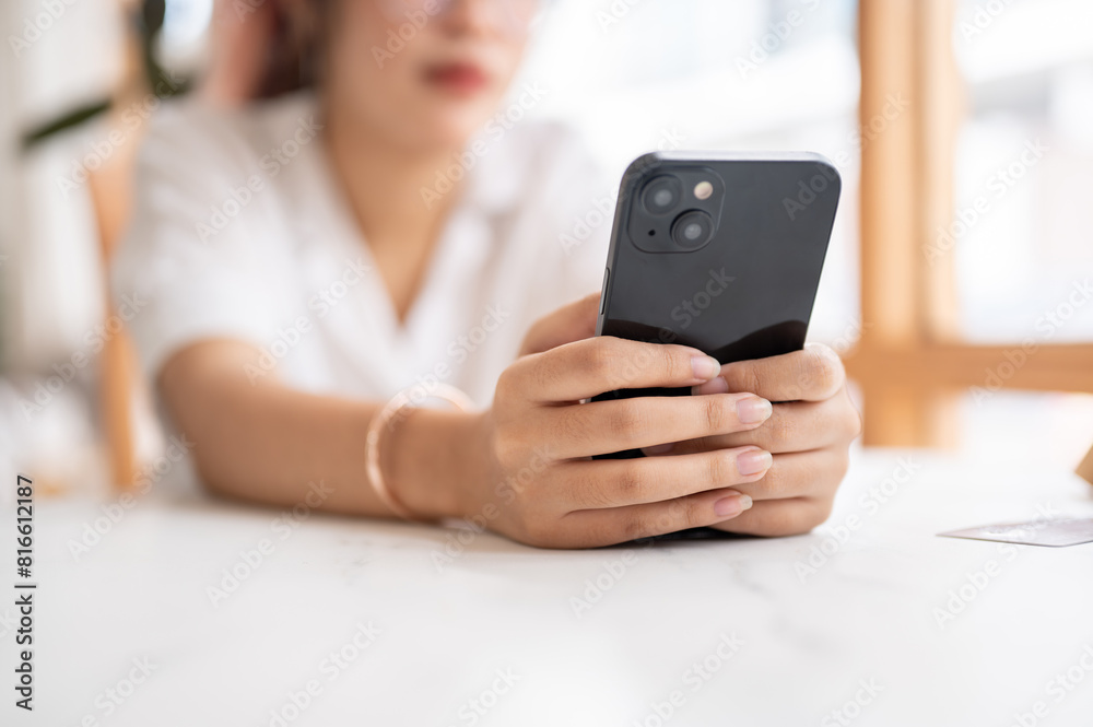 A tired, bored Asian woman leaning on the table and holding her smartphone, waiting for the messages A tired, bored Asian woman leaning on the table and holding her smartphone, waiting for the messages