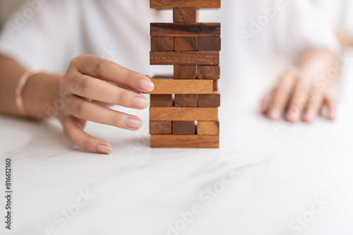 A woman pays her attention on playing a wooden block game at a table, moving a wooden block. photo