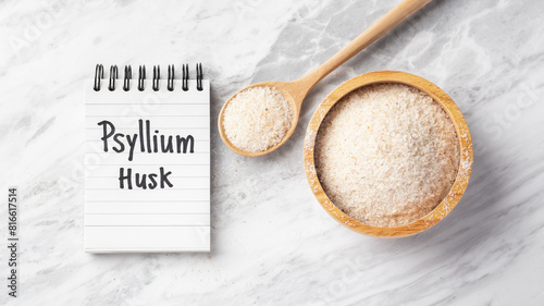Psyllium husk in wooden bowl and spoon with psyllium husk word on notebook on marble table