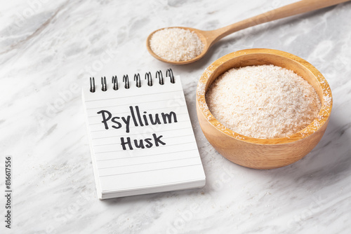 Psyllium husk in wood bowl and spoon with psyllium husk word on notebook on white marble table