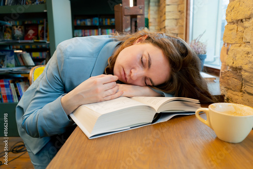 close up in bookstore near the window a beautiful sleepy student is sitting reading books preparing for exams