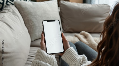 woman holding iphone laying on sofa with white screen mockup and pillow, in the style of use of fabric, clear edge definition