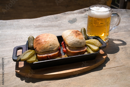 ready to eat - a grilled leberkäs with roasted bread, pickles and a glass of beer served on a wood board on the balcony at a sunny day