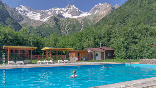 Mom and daughter are swimming in the pool. Relaxing by the water in the fresh air. Sun loungers for relaxing and sunbathing near the blue water pool. Vacation in the mountains in summer.