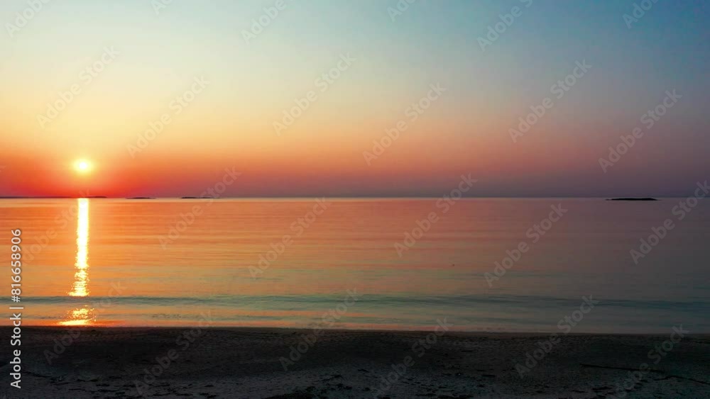 Right Panning View of Gorgeous Beach Sunrise with Bright Glowing Sun Casting Colorful Red Orange Purple and Yellow Reflection Over Peaceful Rippling Waves of the Sea with Beautiful Sky and Ocean Water Right Panning View of Gorgeous Beach Sunrise with Bright Glowing Sun Casting Colorful Red Orange Purple and Yellow Reflection Over Peaceful Rippling Waves of the Sea with Beautiful Sky and Ocean Water