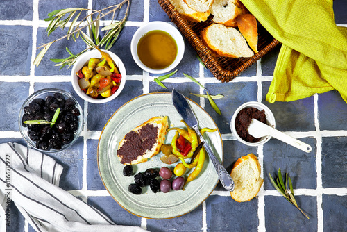Tapenade - paste made from olives. Bowls with spreadable black and green olive cream and oil on tiles background