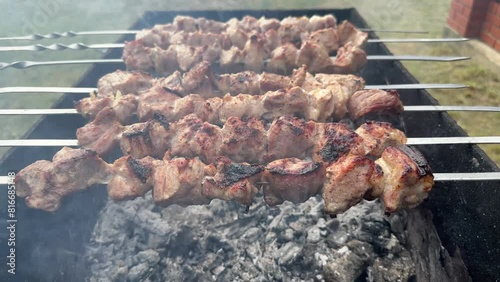 Barbecue grill in the open air. Delicious fried meat on skewers on the brazier. Process of cooking shashlik - meat marinated with spices and onions. Picnic food photo