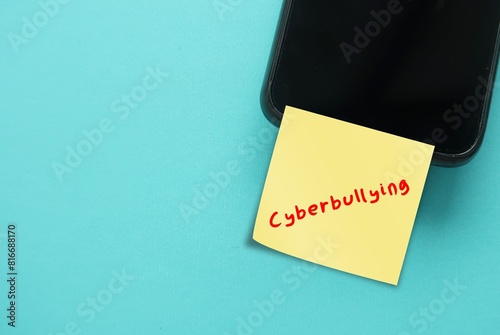Mobile smartphone on copy space background with note written CYBERBULLYING, posting sharing negative, harmful, mean personal content online causing embarrassment humiliation on digital social media