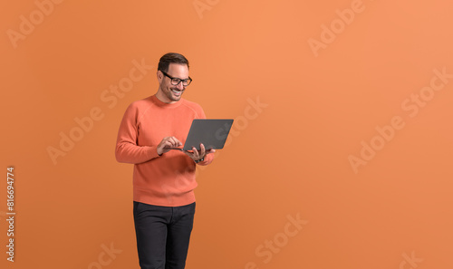 Smiling handsome freelancer working online over wireless computer against isolated orange background
