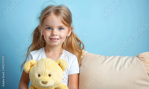 Smiling Young Girl Holding Yellow Teddy Bear Against Soft Blue Background, Perfect Image for Themes of Childhood, Comfort, and Innocence