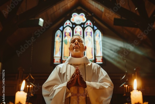 Clergyman prays devoutly in a church, rays of sunlight illuminating him through a colorful stained glass window photo