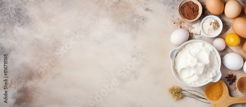 A top down view of ingredients for baking including flour sugar eggs and more arranged on a light stone table with ample room for text or additional images