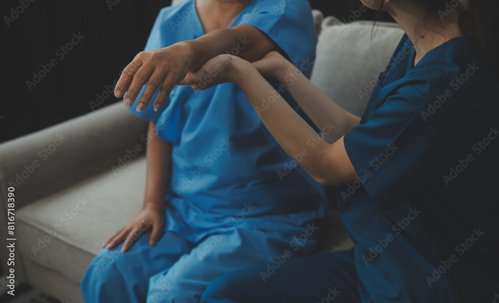 Old woman training with physiotherapist using dumbbells at home. Therapist assisting senior woman with exercises in nursing home. Elderly patient using dumbbells with outstretched arms. Old woman training with physiotherapist using dumbbells at home. Therapist assisting senior woman with exercises in nursing home. Elderly patient using dumbbells with outstretched arms.
