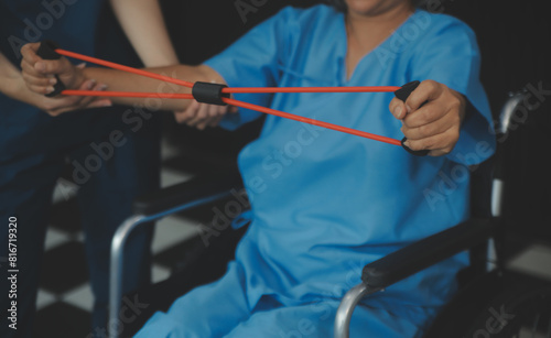 Personal trainer assisting senior woman with resistance band. Rehabilitation physiotherapy worker helping old patient at nursing home. Old woman with stretch band being coached by physiotherapist.