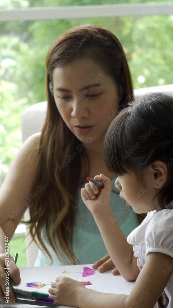 A young, Asian child work and play at home with her mother learning to read and write in the cozy comfort of their living room A young, Asian child work and play at home with her mother learning to read and write in the cozy comfort of their living room
