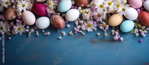 Top view of a colorful Easter egg composition featuring natural dyed eggs and gypsophila on a colored table providing ample copy space in the background