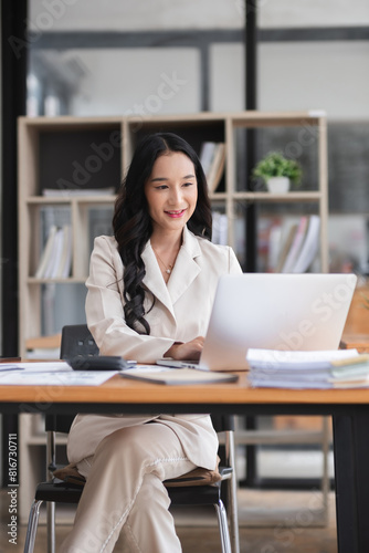 Asian businesswoman working on financial document with laptop on desk in office room
