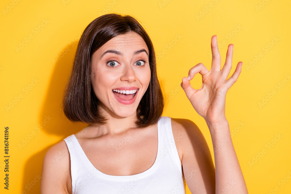 Photo of funky excited lady dressed white top smiling showing okey sign isolated yellow color background Photo of funky excited lady dressed white top smiling showing okey sign isolated yellow color background