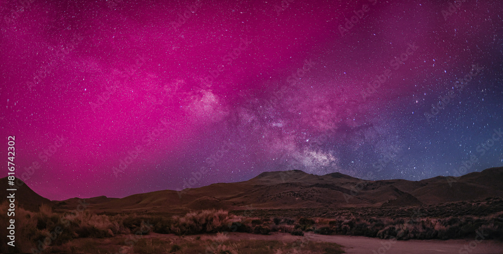 The Milky Way visible through the Aurora Borealis over a mountainous landscape at night