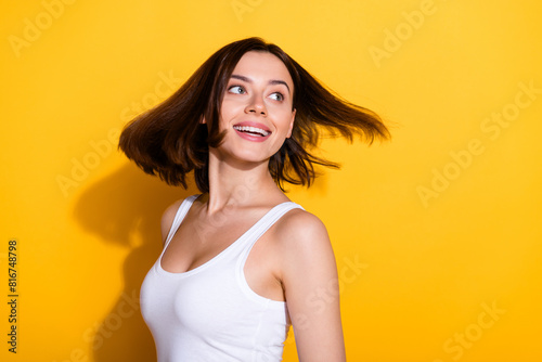 Photo portrait of attractive young girl fluttering hair look empty space wear trendy white outfit isolated on yellow color background