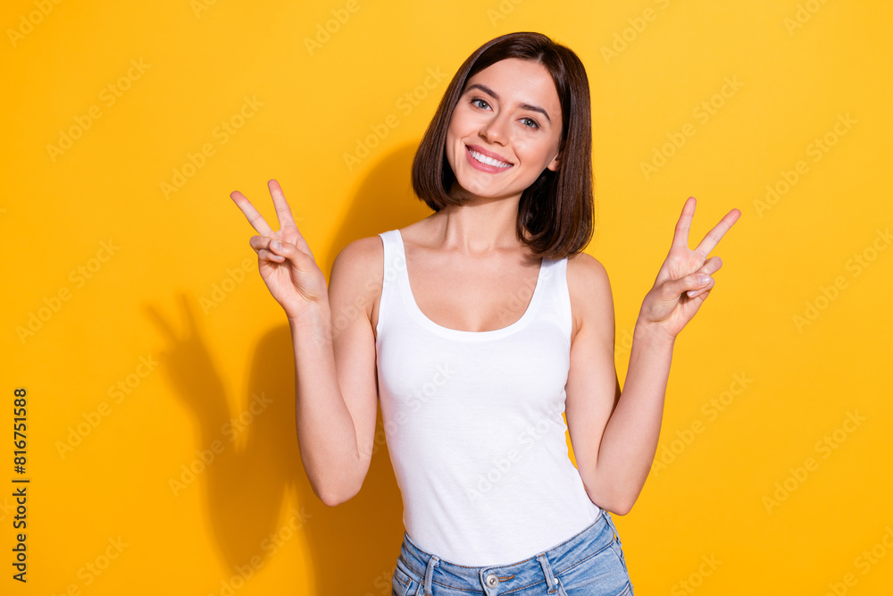 Photo portrait of attractive young girl show v-sign wear trendy white outfit isolated on yellow color background Photo portrait of attractive young girl show v-sign wear trendy white outfit isolated on yellow color background