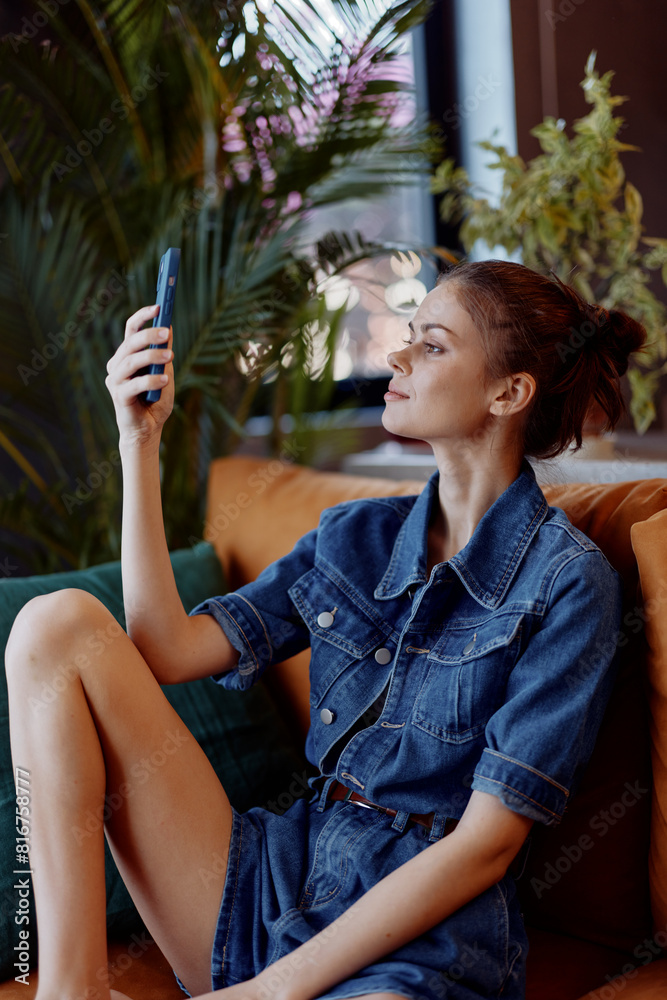 Young woman sitting on a comfortable sofa with a smartphone in hand, deeply focused on the screen Young woman sitting on a comfortable sofa with a smartphone in hand, deeply focused on the screen