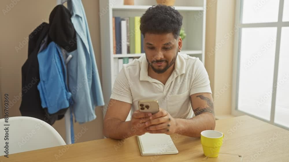 Handsome man texting indoors with coffee and notebook on the table, exuding casual coziness at home. Handsome man texting indoors with coffee and notebook on the table, exuding casual coziness at home.