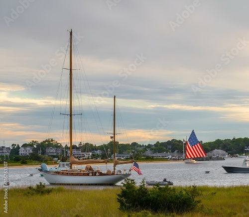 Fotografie Catboat with American Flag sails by boats in Edgartown Harbor on the island of M