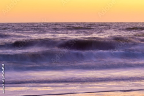 two surfers walk on a beach during a beautiful sunset