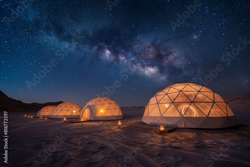 Four dome tents illuminated from within stand in the desert under a starry sky