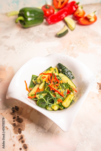 Fresh cucumbers, bell peppers, and herbs on white plate, pink background