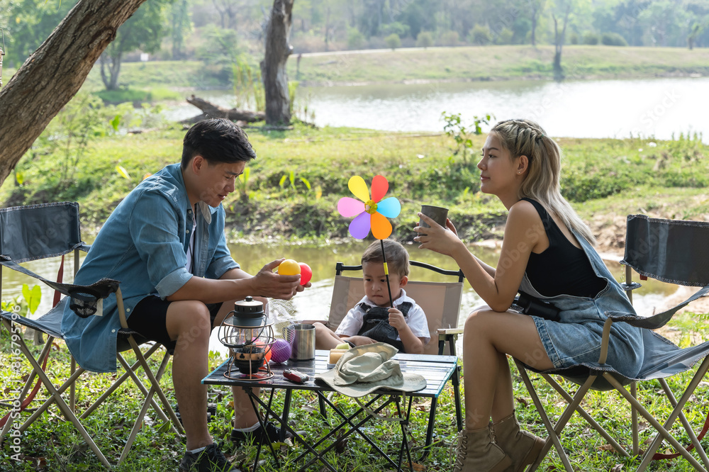 Obraz premium Young Asian family with father mother and son sitting on camping chair in camp site