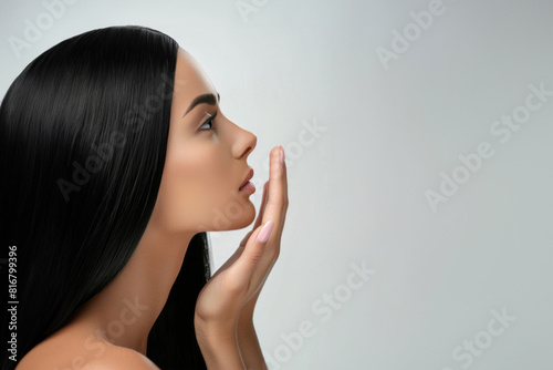 Profile View of a Woman With Long Black Hair Touching Her Face Against Plain Background