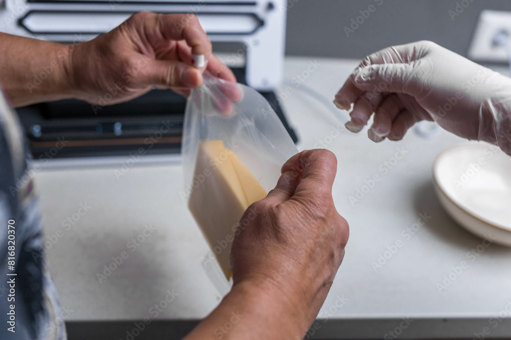 Close-up of men's hands sealing cheese into an airtight bag using a vacuum sealer Close-up of men's hands sealing cheese into an airtight bag using a vacuum sealer