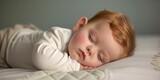 A cute ginger baby is sleeping on a white blanket.