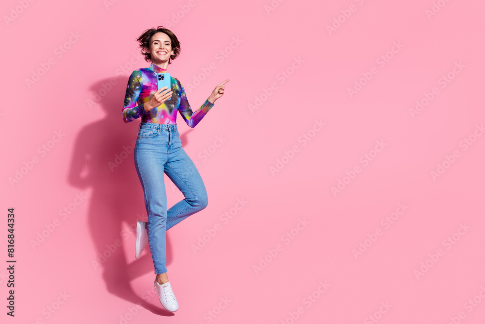 Full size photo of nice girl smart phone wear pullover jump point finger empty space isolated on pink color background Full size photo of nice girl smart phone wear pullover jump point finger empty space isolated on pink color background