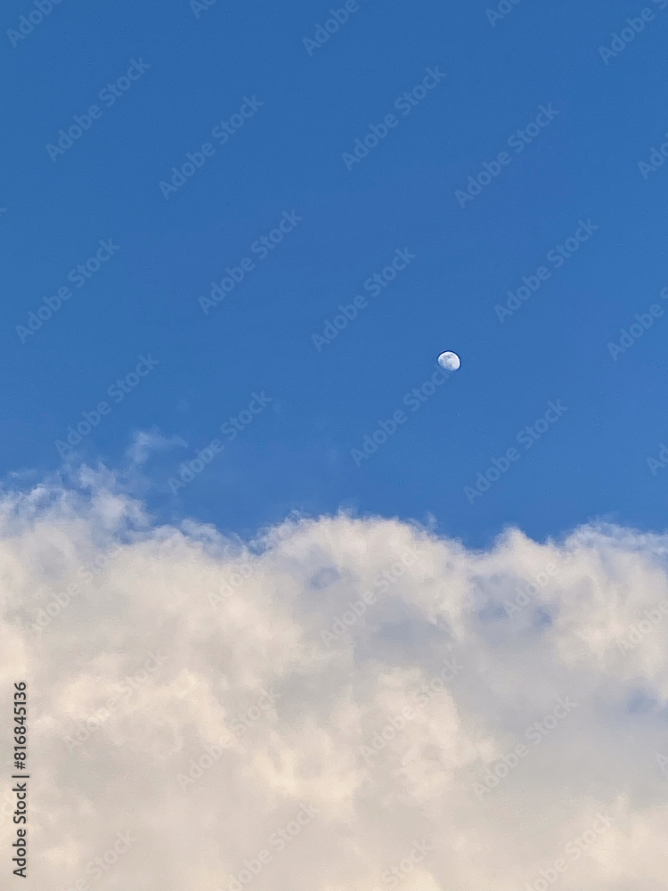 Bright blue sky with fluffy white clouds and the moon in the daytime. Beautiful and serene natural view capturing celestial tranquility Bright blue sky with fluffy white clouds and the moon in the daytime. Beautiful and serene natural view capturing celestial tranquility