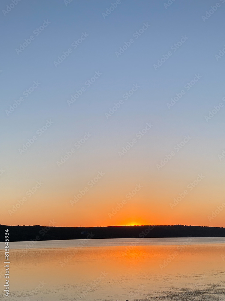 Stunning sunset over a tranquil lake, with vibrant orange and pink hues reflecting in the water. Serene landscape view for peaceful moments Stunning sunset over a tranquil lake, with vibrant orange and pink hues reflecting in the water. Serene landscape view for peaceful moments