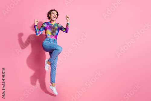 Full size photo of nice young woman raise fists jump empty space wear pullover isolated on pink color background