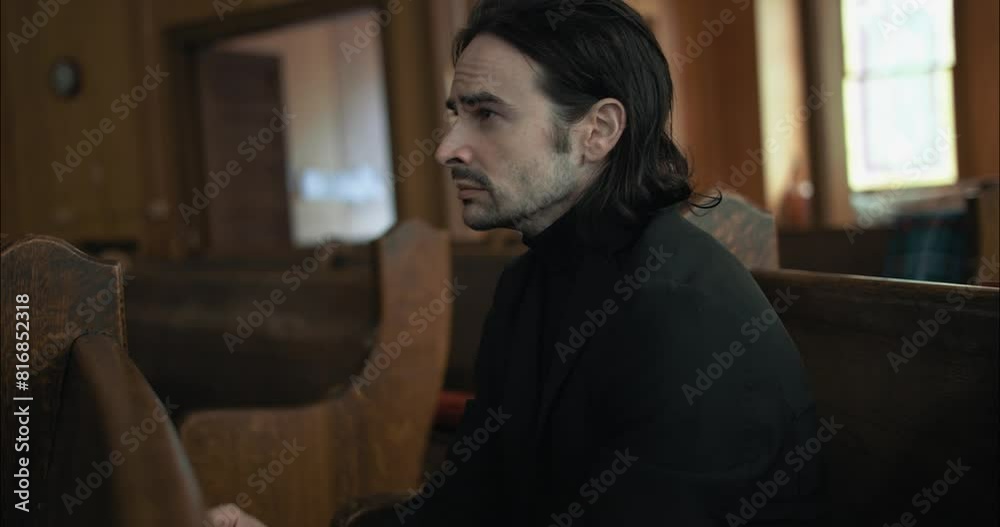 Young man in black suit sitting in pew in church praying in worship in cinematic slow motion. Young man in black suit sitting in pew in church praying in worship in cinematic slow motion.