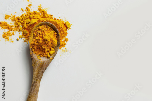 Wooden spoon overflowing with vibrant yellow turmeric powder on a clean white background with a minimalist design photo