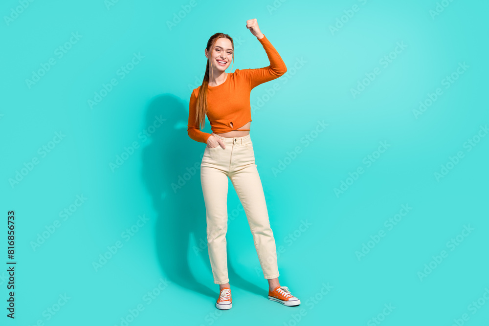 Full size photo of satisfied girl with ginger hair dressed orange shirt raising fist up win betting isolated on teal color background Full size photo of satisfied girl with ginger hair dressed orange shirt raising fist up win betting isolated on teal color background